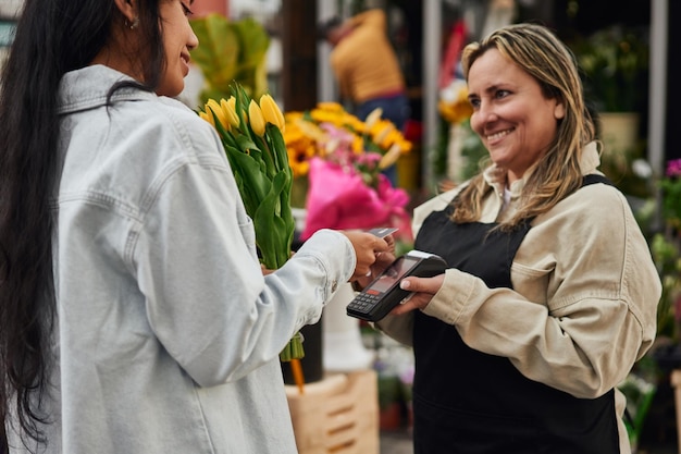 Young Latina woman purchasing vibrant flowers and plants from a street vendor's stall