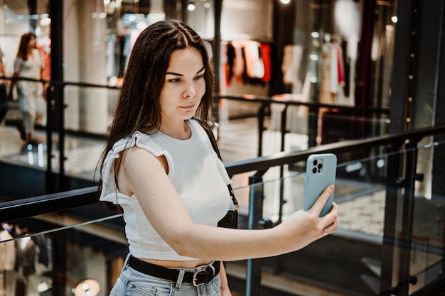 Young latina woman with shopping bags using her smart phone while standing in shopping center mall