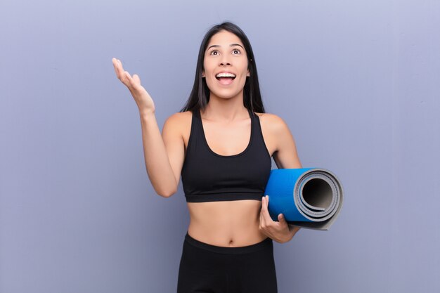 Young lating woman with a yoga mat on cement wall