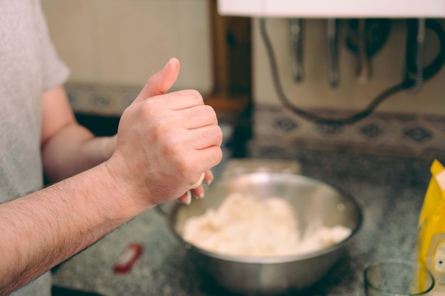 Young latino hispanic man kneading arepas on the kitchen counter with arepa dough in a bowl at the background