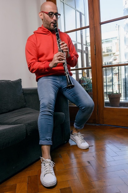 young latino man at home sitting on the couch playing the clarinet