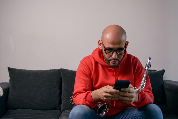 young latino man musician sitting at home checking the phone looking for sheet music online