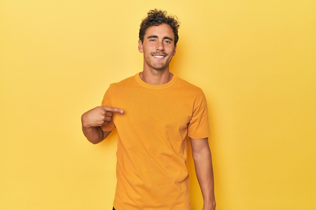 Young latino man posing on yellow background person pointing by hand to a shirt copy space