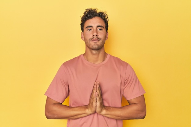 Young Latino man posing on yellow background praying showing devotion religious person looking for divine inspiration
