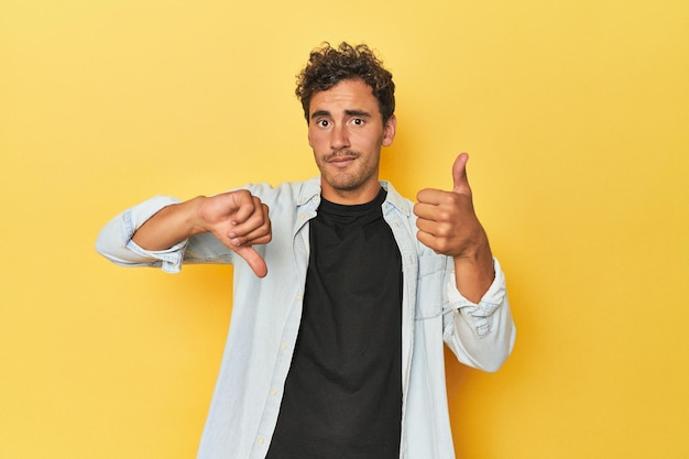 Photo young latino man posing on yellow background showing thumbs up and thumbs down