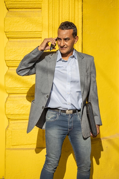 Young latino man talking on the mobile phone isolated on yellow background