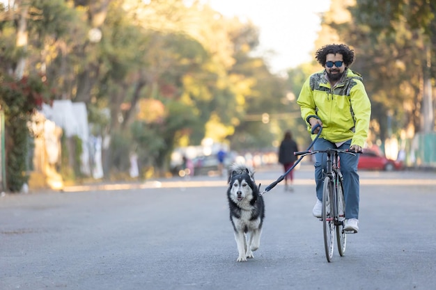 Молодой латиноамериканский мужчина в солнцезащитных очках едет на велосипеде со своей собакой