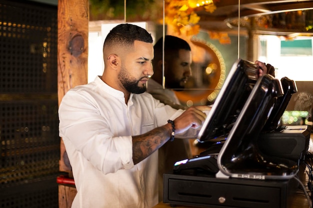 Young Latino worker in small business preparing the bill at the cash register. Space for text.