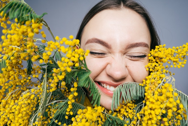 若い笑っている女の子は、香りのよい黄色のミモザ、春の花を嗅ぎます