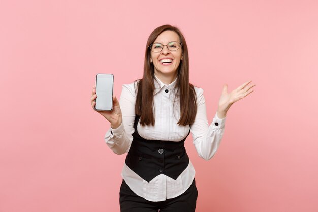 빈 화면이 있는 휴대폰을 들고 분홍색 배경에 격리된 손을 펼치고 있는 정장 안경을 쓴 성공적인 비즈니스 여성이 웃고 있습니다. 여사장님. 성취 경력 부입니다. 공간을 복사합니다.