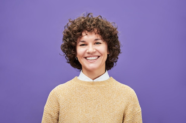Young laughing woman with shoert curly brown hair looking at camera