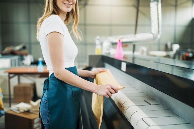 Young laundry worker pats the linen on the automatic machine at the dry cleaners.