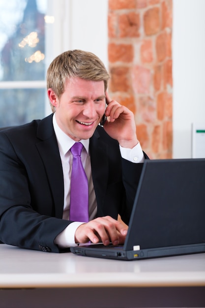 Молодой юрист, работающий в своем офисе, он сидит на столе и по телефону является клиентом или клиентом