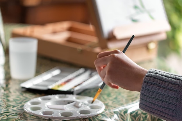 Young lefthanded girl painting still life with flowers mixing watercolor paint in palette