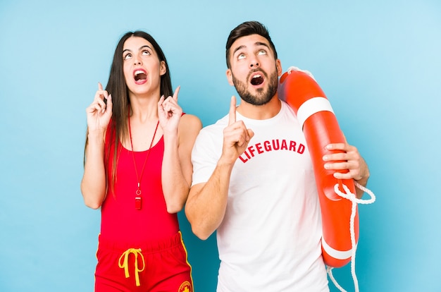 Young lifeguard couple isolated pointing upside with opened mouth.