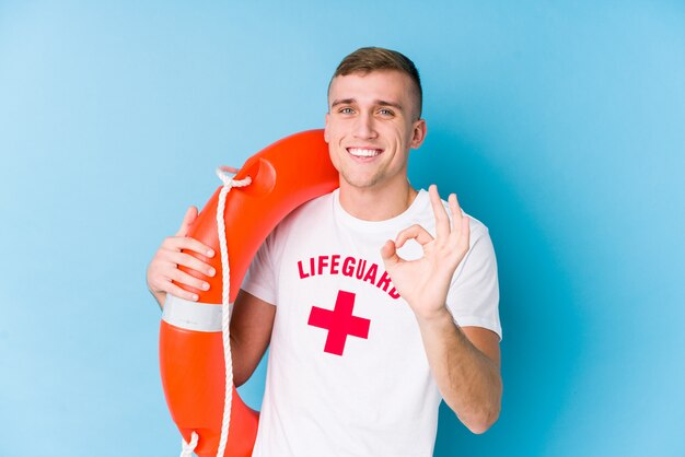 Young lifeguard man holding a rescue float cheerful and confident showing ok gesture.