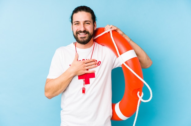 Young lifeguard man holding a rescue float laughs out loudly keeping hand on chest.