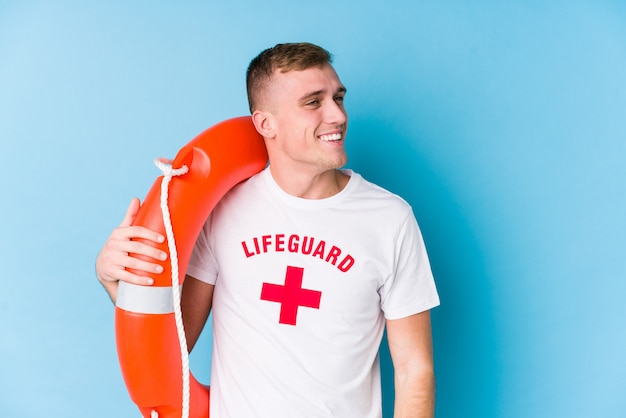 Young lifeguard man holding a rescue float looks aside smiling, cheerful and pleasant.