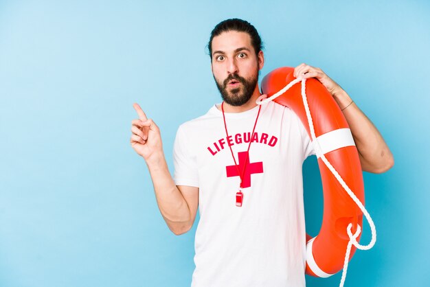 Young lifeguard man holding a rescue float pointing to the side