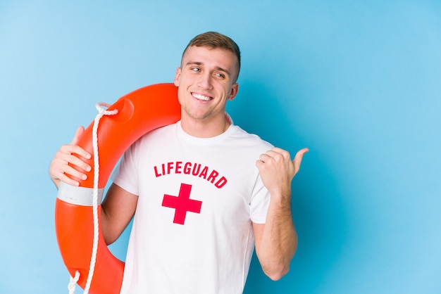 Young lifeguard man holding a rescue float points with thumb finger away, laughing and carefree.