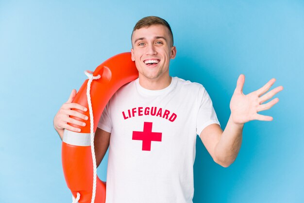 Young lifeguard man holding a rescue float receiving a pleasant surprise, excited and raising hands.