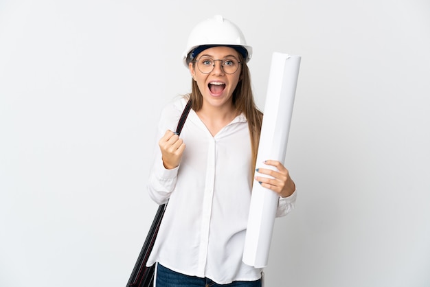 Young Lithuanian architect woman with helmet and holding blueprints isolated on white wall celebrating a victory in winner position