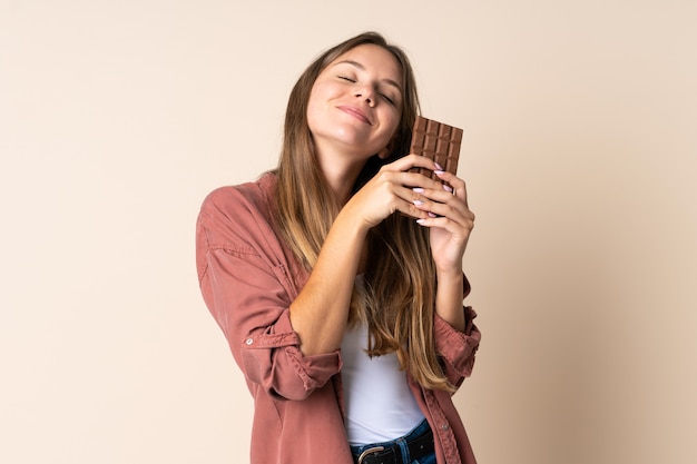 Young Lithuanian woman on beige taking a chocolate tablet and happy