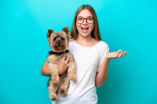 ショックを受けた顔の表情で青い背景で隔離の犬を保持している若いリトアニアの女性