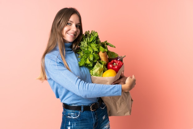 Young Lithuanian woman holding a grocery shopping bag pointing back