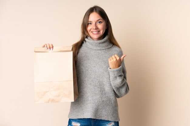 Young Lithuanian woman holding a grocery shopping bag pointing to the side to present a product