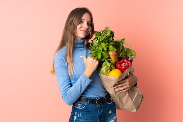 Young Lithuanian woman holding a grocery shopping bag proud and self-satisfied