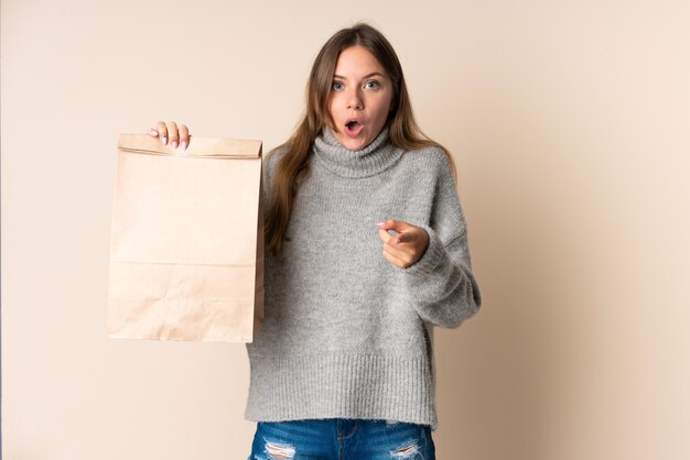 Young Lithuanian woman holding a grocery shopping bag surprised and pointing front