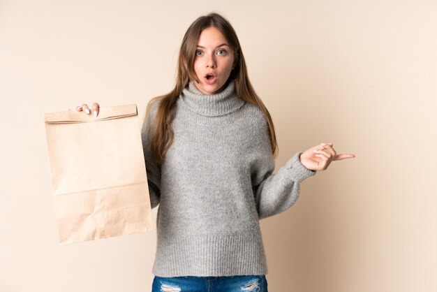 Young Lithuanian woman holding a grocery shopping bag surprised and pointing side