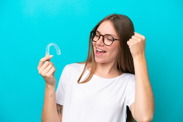 Young Lithuanian woman holding invisible braces isolated on blue background celebrating a victory