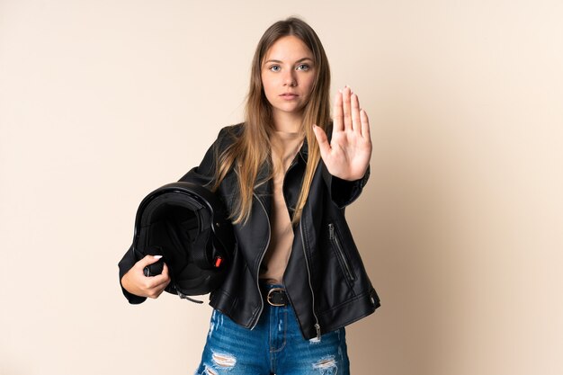 Young Lithuanian woman holding a motorcycle helmet on beige making stop gesture