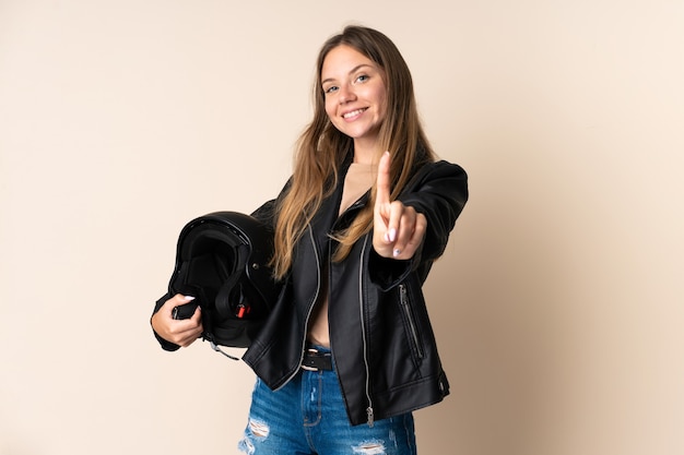 Young Lithuanian woman holding a motorcycle helmet isolated on beige background showing and lifting a finger