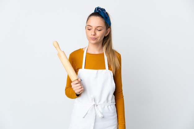 Young Lithuanian woman holding a rolling pin isolated on white background having doubts while looking side