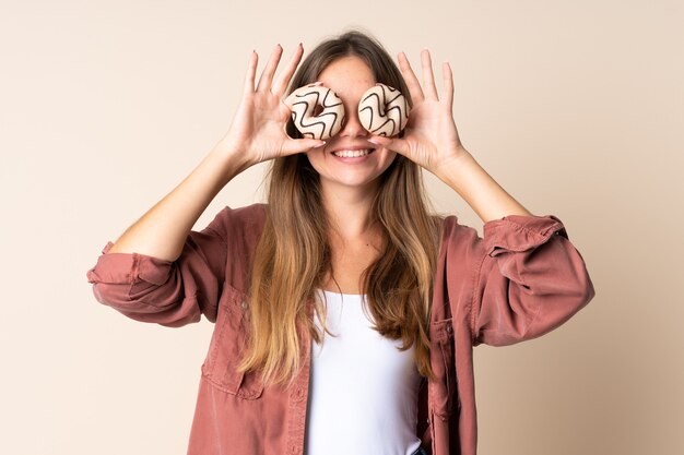 Foto giovane donna lituana isolata su fondo beige che tiene le ciambelle negli occhi