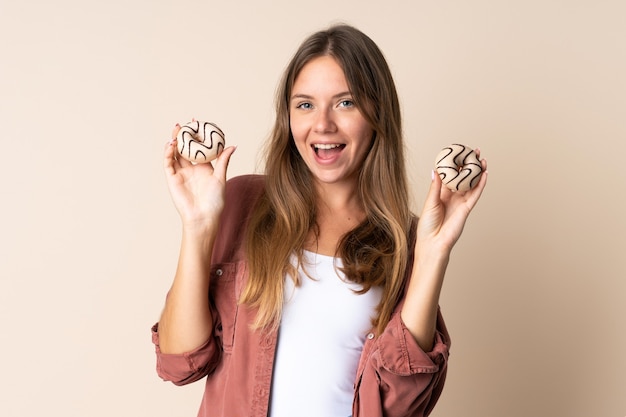 Young Lithuanian woman isolated on beige holding donuts with happy expression