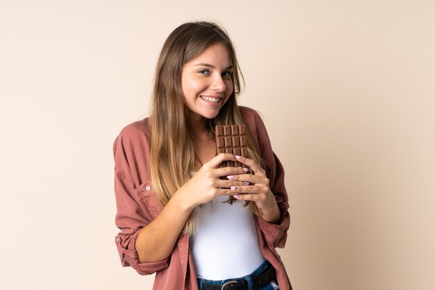 Young Lithuanian woman isolated on beige taking a chocolate tablet and happy