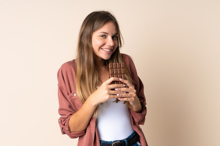 Photo young lithuanian woman isolated on beige taking a chocolate tablet and happy