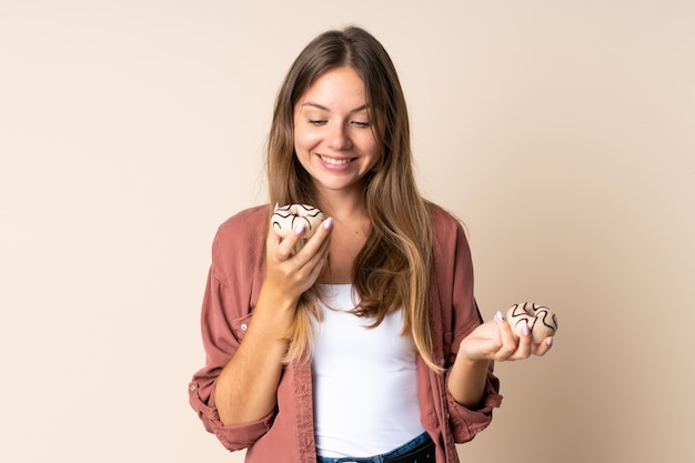 행복 한 표정으로 도넛을 들고 베이지 색 벽에 고립 된 젊은 리투아니아 여자