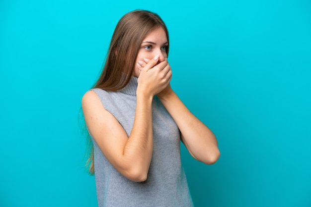 Young Lithuanian woman isolated on blue background covering mouth and looking to the side