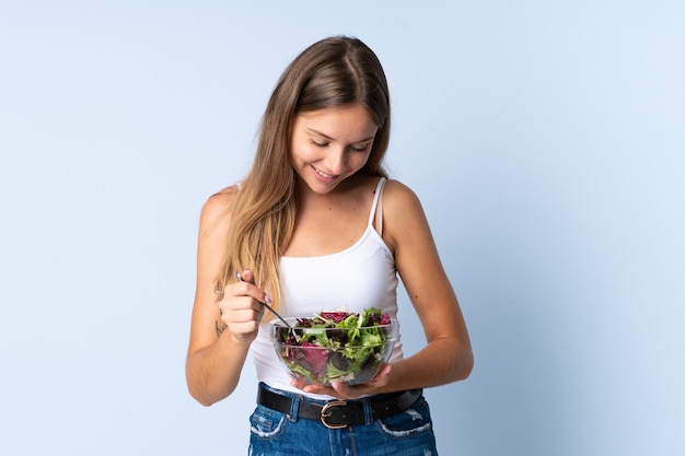 Young Lithuanian woman isolated on blue background holding a bowl of salad with happy expression