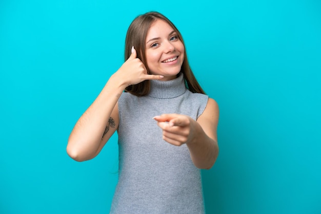 若いリトアニアの女性は、電話のジェスチャーをし、正面を指して青い背景に分離