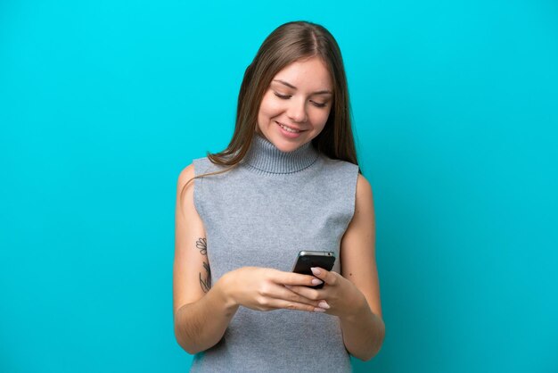 Young Lithuanian woman isolated on blue background sending a message with the mobile