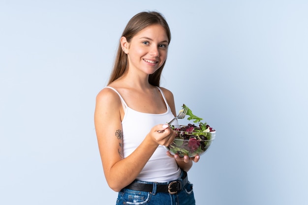 Giovane donna lituana isolata sull'azzurro che tiene una ciotola di insalata con l'espressione felice