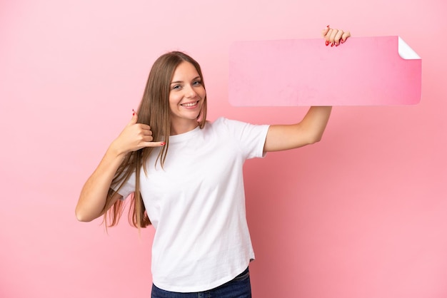 Young Lithuanian woman isolated on pink background holding an empty placard and doing phone gesture