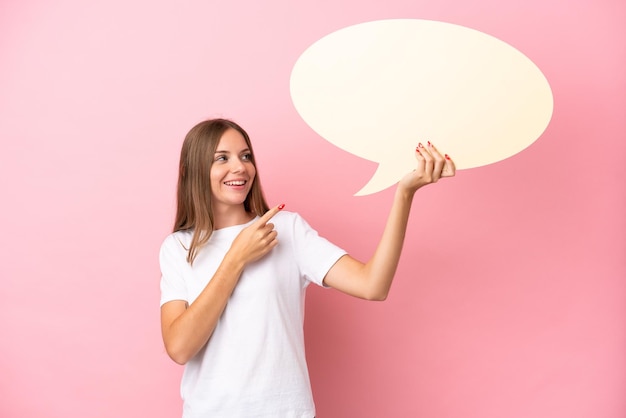 Young Lithuanian woman isolated on pink background holding an empty speech bubble and pointing it