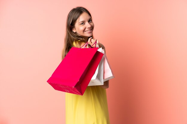 Young Lithuanian woman isolated on pink wall holding shopping bags and smiling